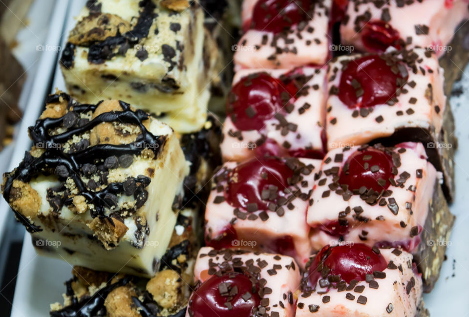 Closeup of gourmet vanilla, cherry and chocolate fudge with fancy sprinkles decoration and cherry garnish on tray ready to eat homemade dessert photography background 