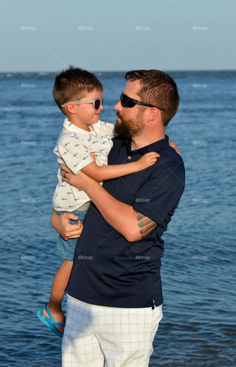 Father holding son on the shore of the beach and smiling together