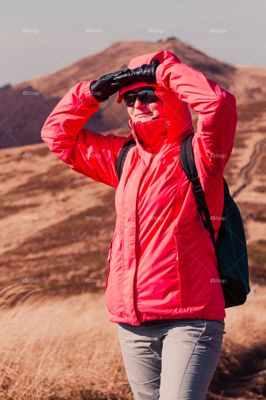 Woman admiring mountains scenery during a trip in the mountains on sunny windy autumn day. Hiker wearing sports clothes. There is grassy hillside coloured with browns in the background