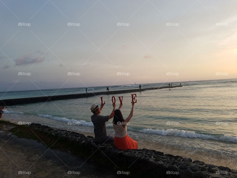 a couple spells the word love while posing in front of Waikiki Sunset