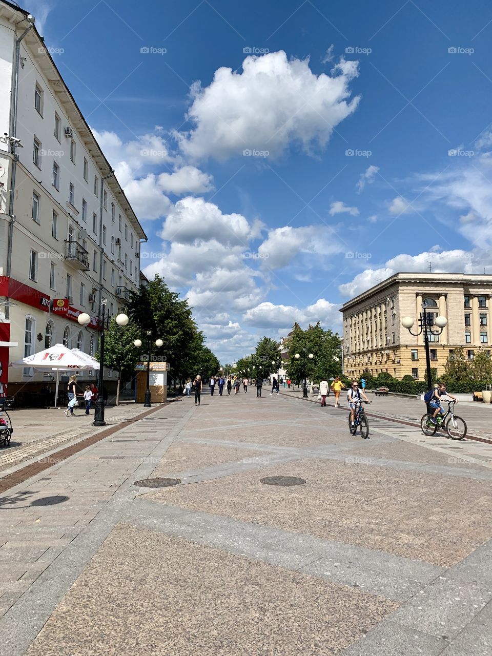 City street on a summer day. There are white clouds in the sky. people walk and ride bicycles