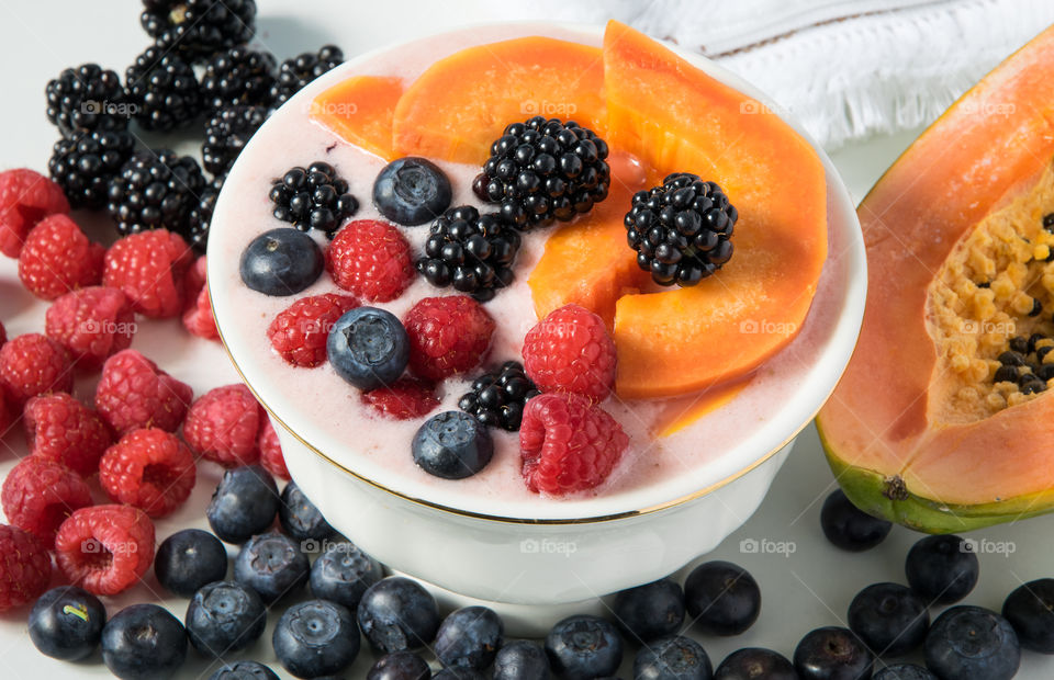 Bowl of yoghurt and fruit smoothie topped with papaya and berries