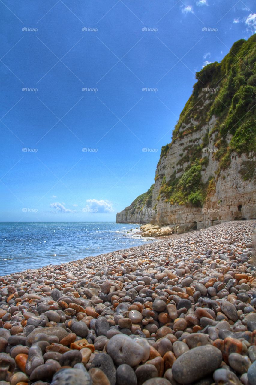 A pebble beach and rugged cliffs under a bright blue sky.