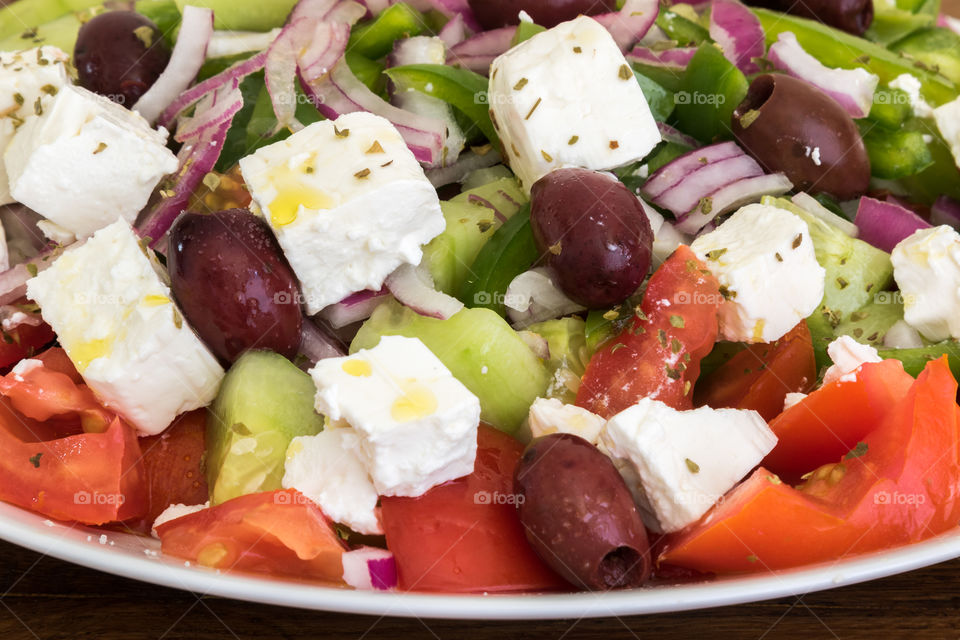 a detailed view of a homemade Greek salad. the main ingredients are tomatoes, cucumber, feta cheese, green pepper and kalamata olives.
