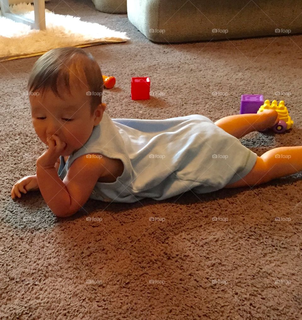 Eight month old baby boy on the floor crawling with fingers in mouth.