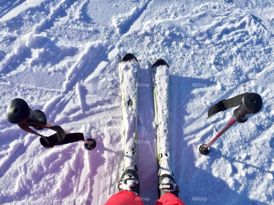 Looking down at feet wearing skis with ski poles beside