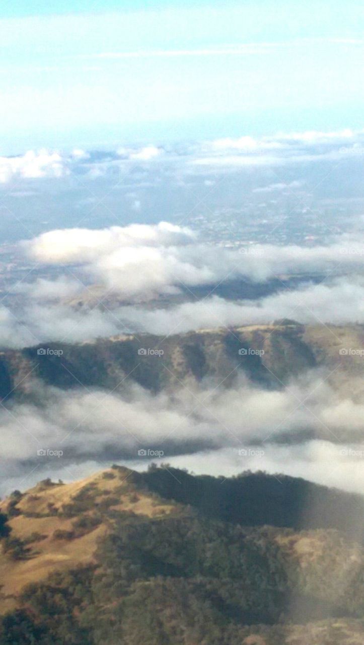 Beautiful CA. mountains under blue-gray-white clouds, seen through  plane window