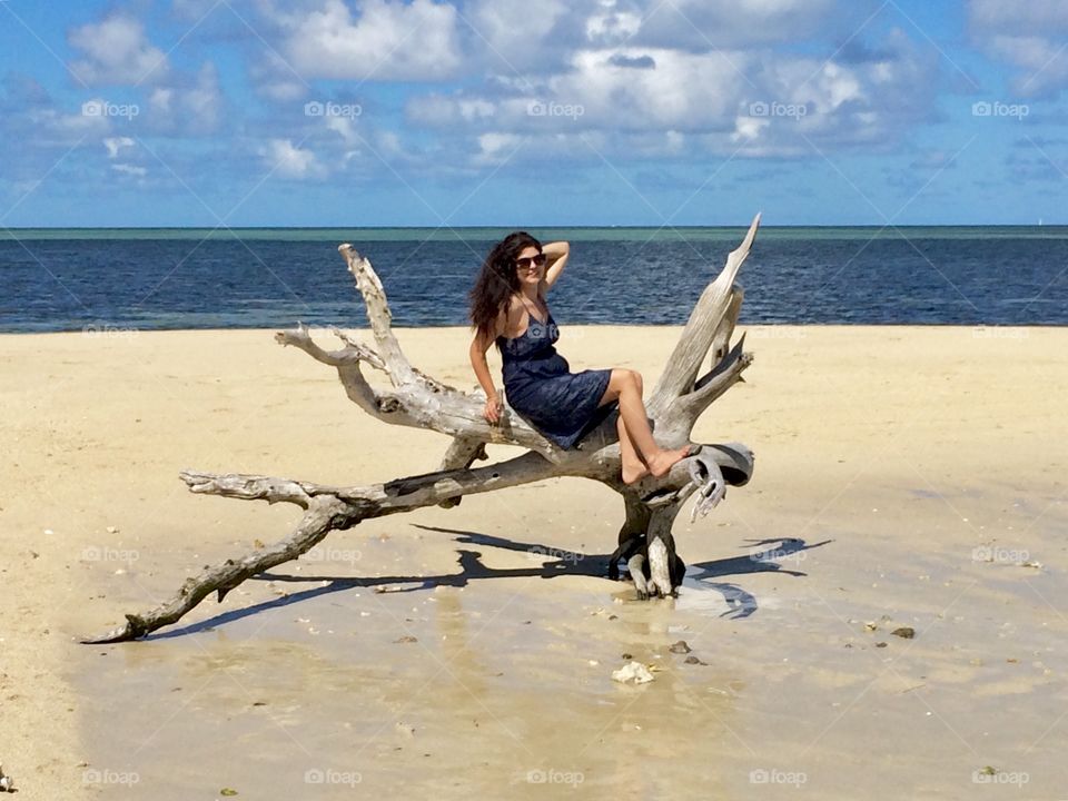 Young woman posing on a dead wood on a paradise beach on a desert island of Pacific ocean 