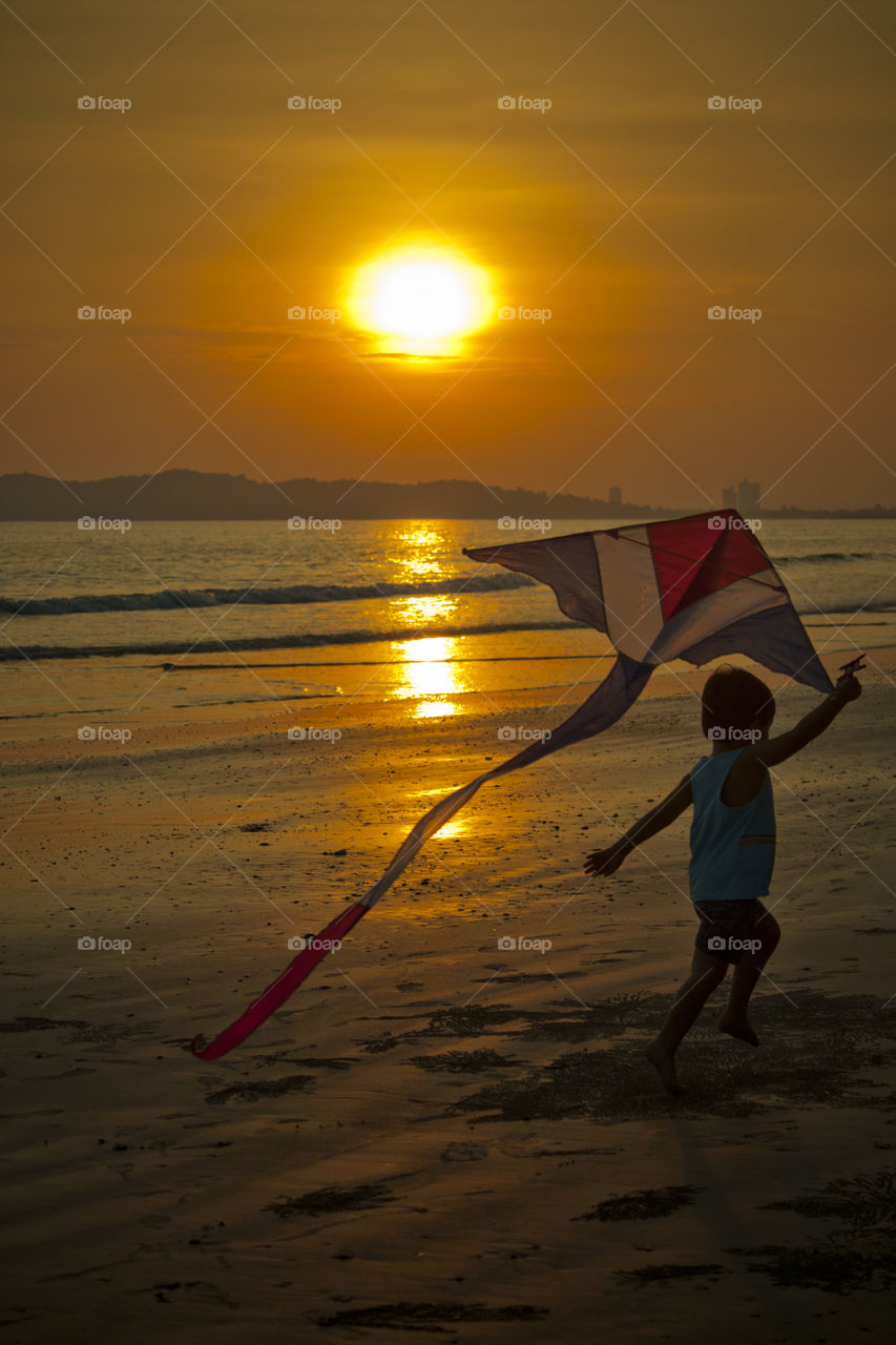 young boy running on the beach during sunset . Thitiwin Dupont