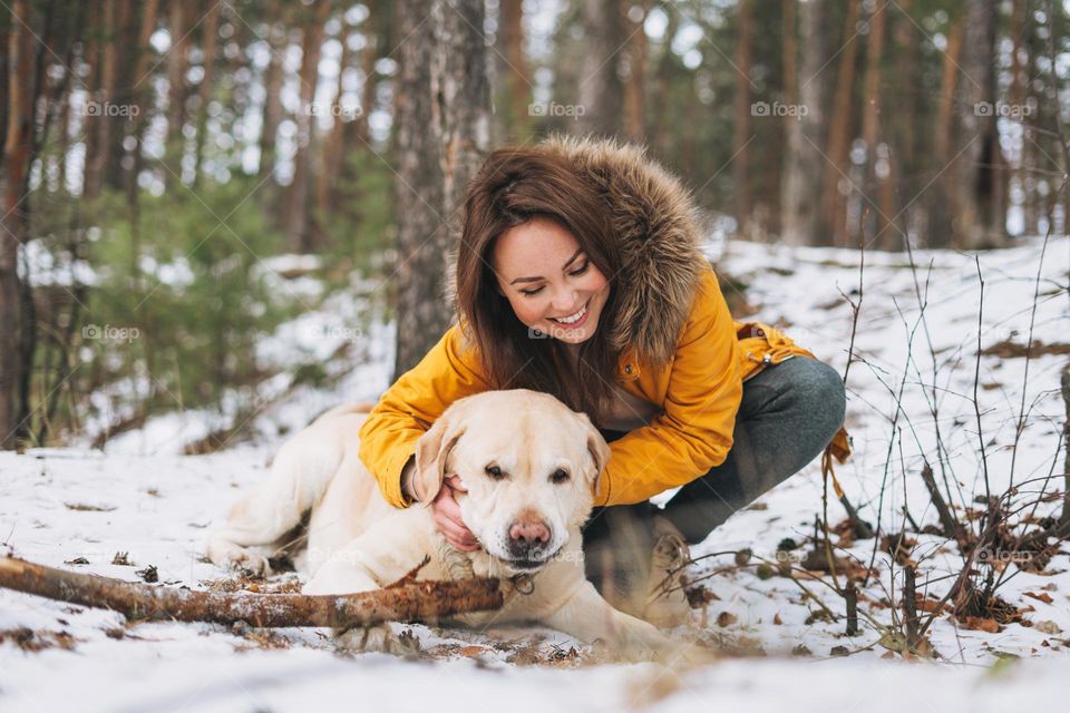 Young smiling woman in yellow jacket with big kind white dog Labrador walking in the winter forest