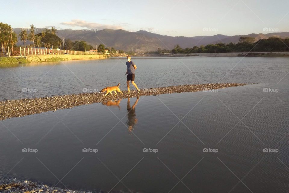 A man walking his dog near a river a the sea during sunset