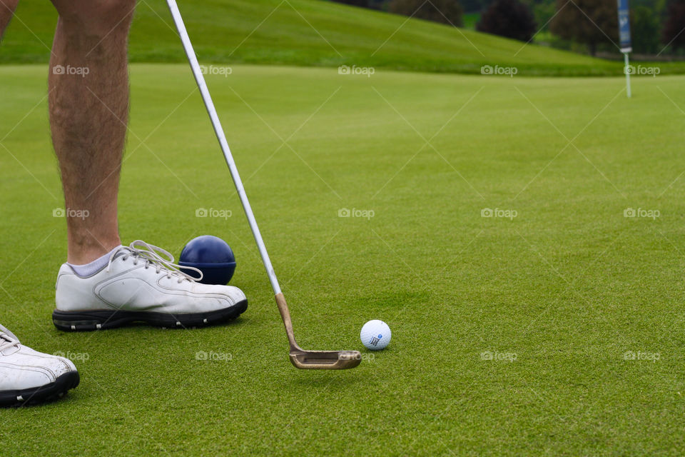 A golfer putts a ball along the beautiful green fairway towards the hole with shoes in frame