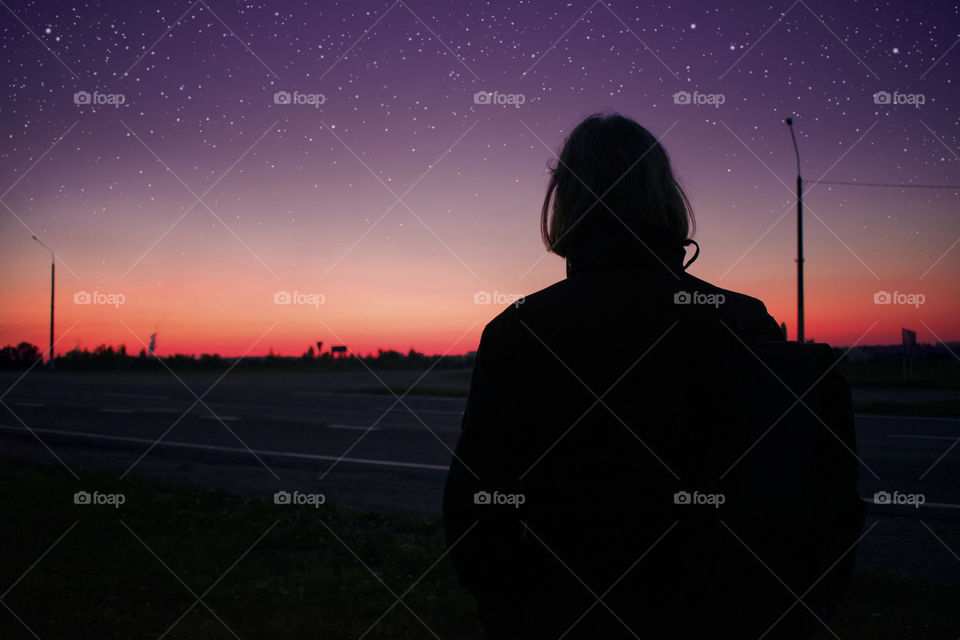 Dark silhouette of a young man looking on the stars and beautiful colorful sundown. Night time, underexposed picture.