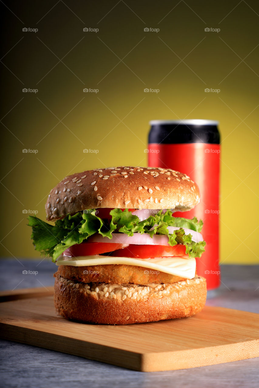 Fast food burger on a wooden board with cold drink can