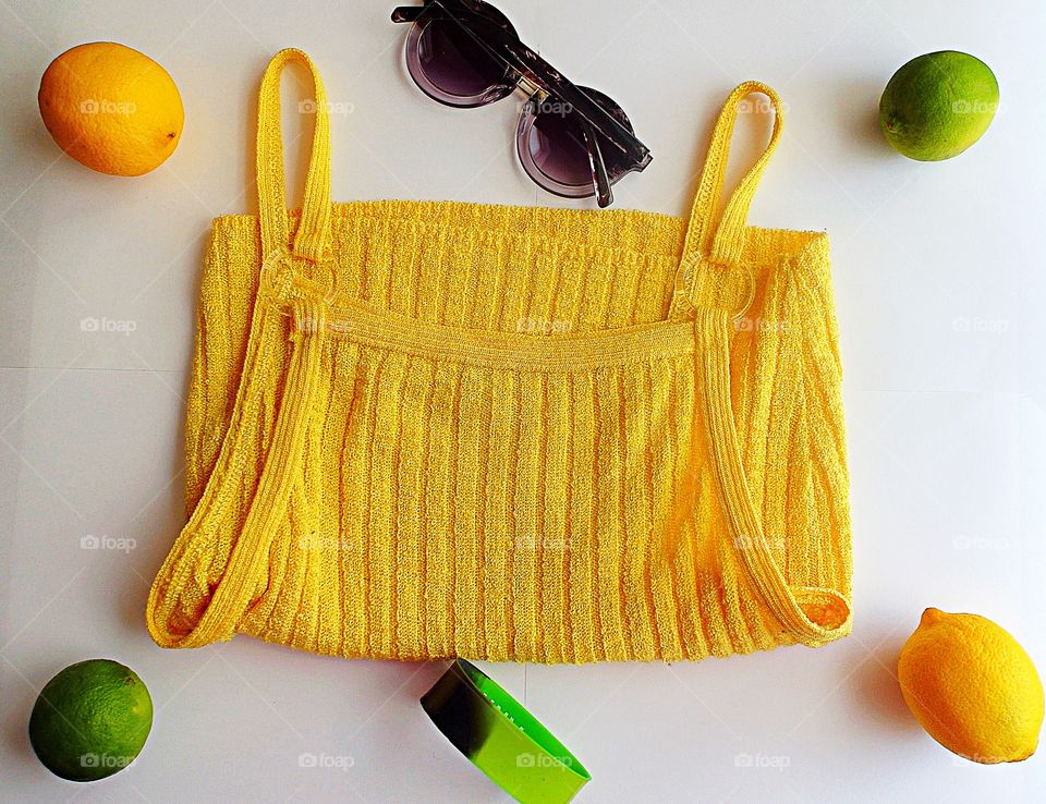 Yellow tank top with sunglasses, a bracelet, limes and lemons on a white background 