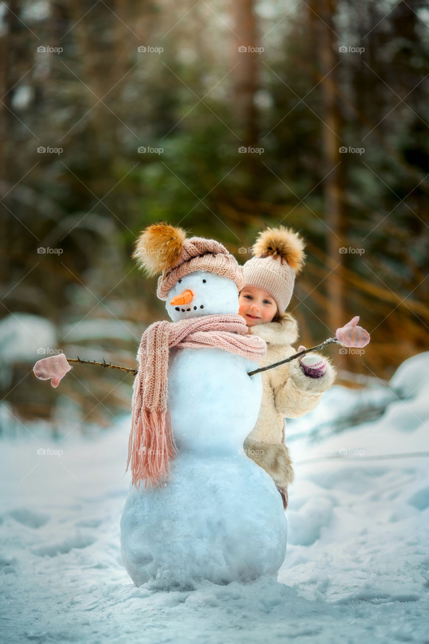 Little girl with snowman in winter forest at sunny day