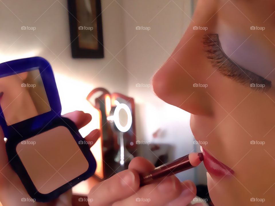 Woman using a mirror to apply lipstick to her rose colored lips.