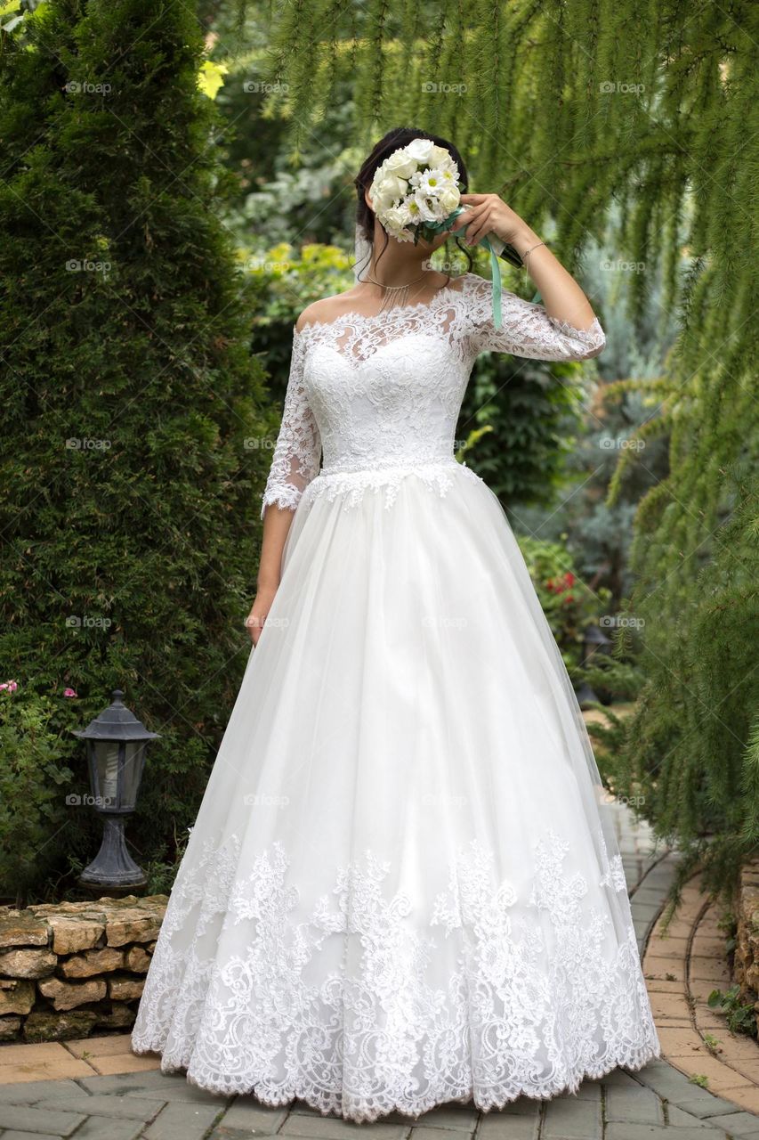 Bride in wedding dress hiding her face with wedding bouquet 