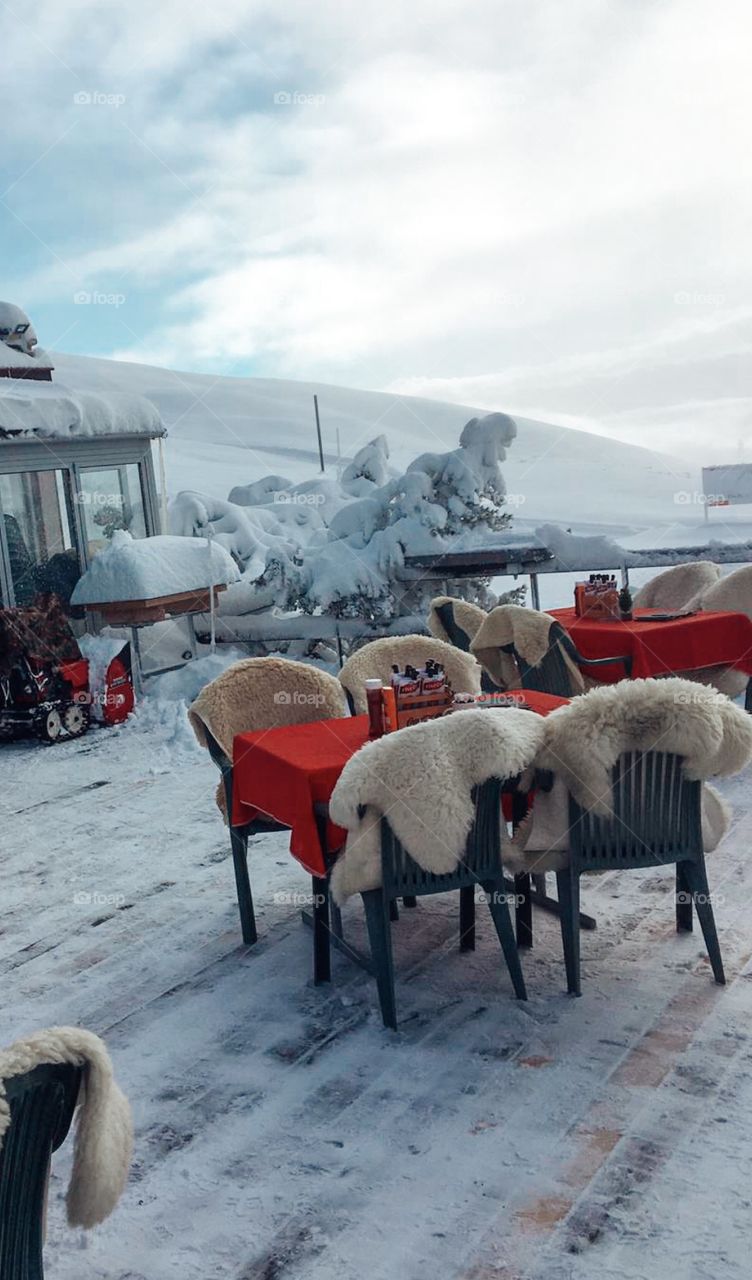 Tables and chairs outside a restaurant in winter . A lot of white snow . on a mountain 