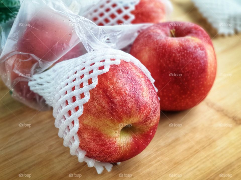 Fresh apples from a supermarket come with SINGLE-USE PLASTICS grocery bag and fruit foam net. Environmentalism & Plastic Awareness.