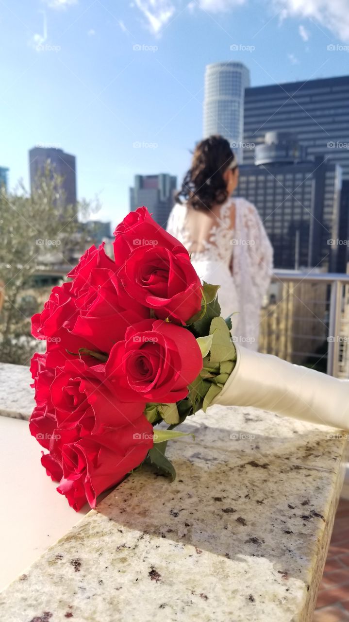 Bride gazing over Downtown Los Angeles with bouquet of red roses