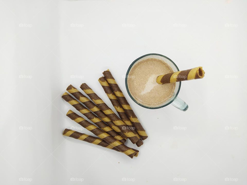 Some wafer roll sticks and a glass of chocolate milk on white background. Top view