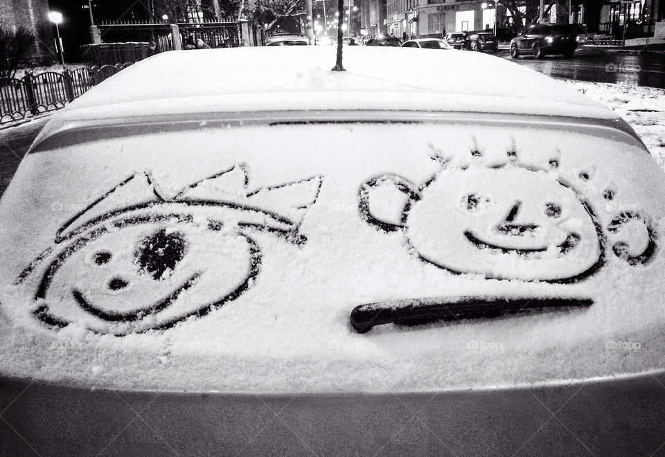 Finger drawings of children faces on the car glass covered with snow. Black and white.