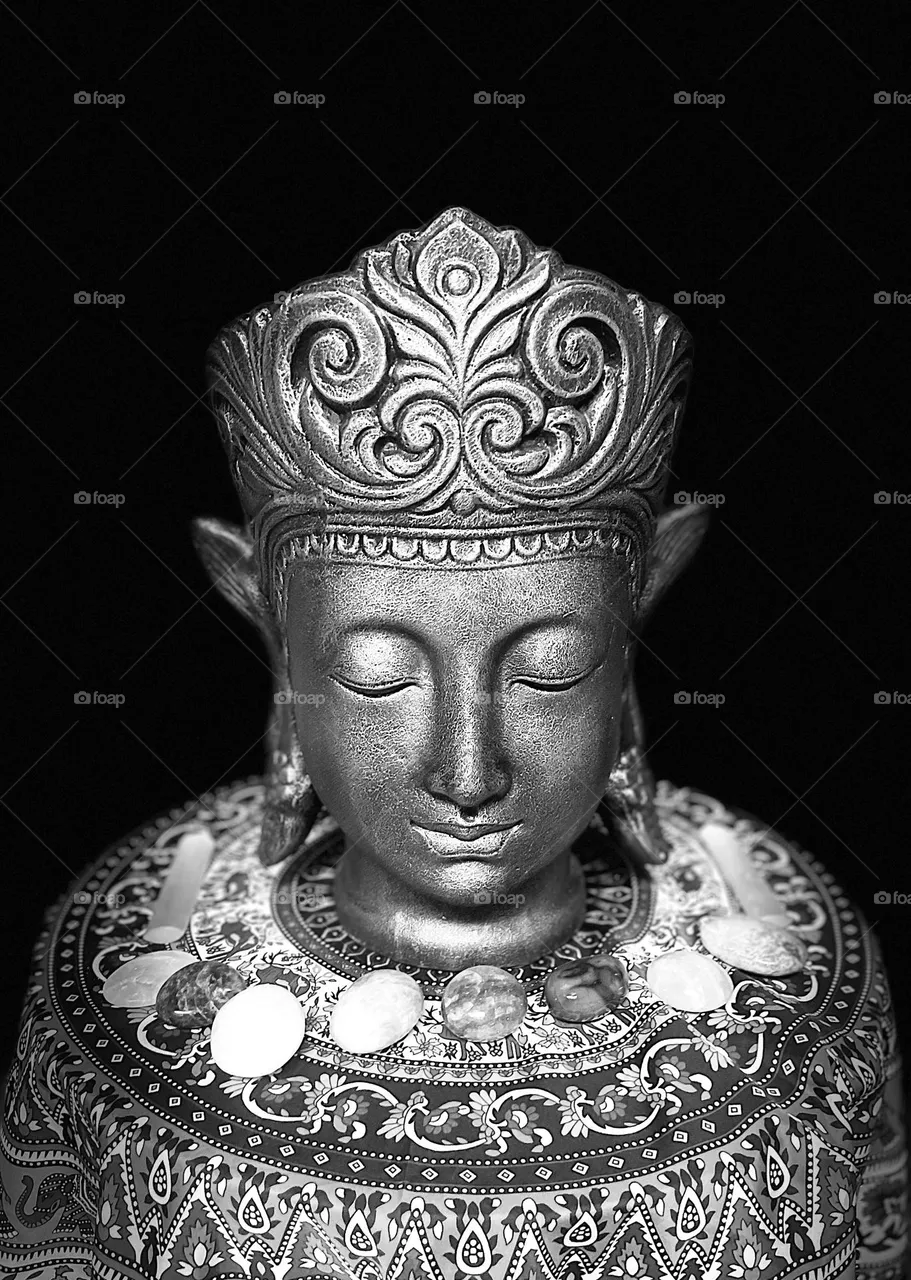 A black and white photo of a Buddha meditating with crystals in the dark.