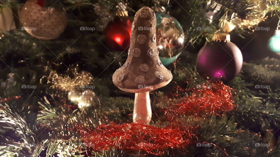 Christmastree decoration. Silver mushroom ornament clipped onto green branch surounded by red angels hair.