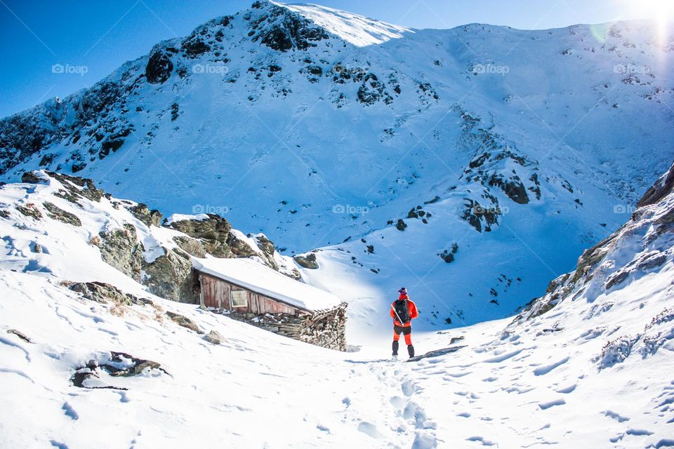 Amazing view of a hiker standing next to a mountain refugee in the winter on a bluebird day