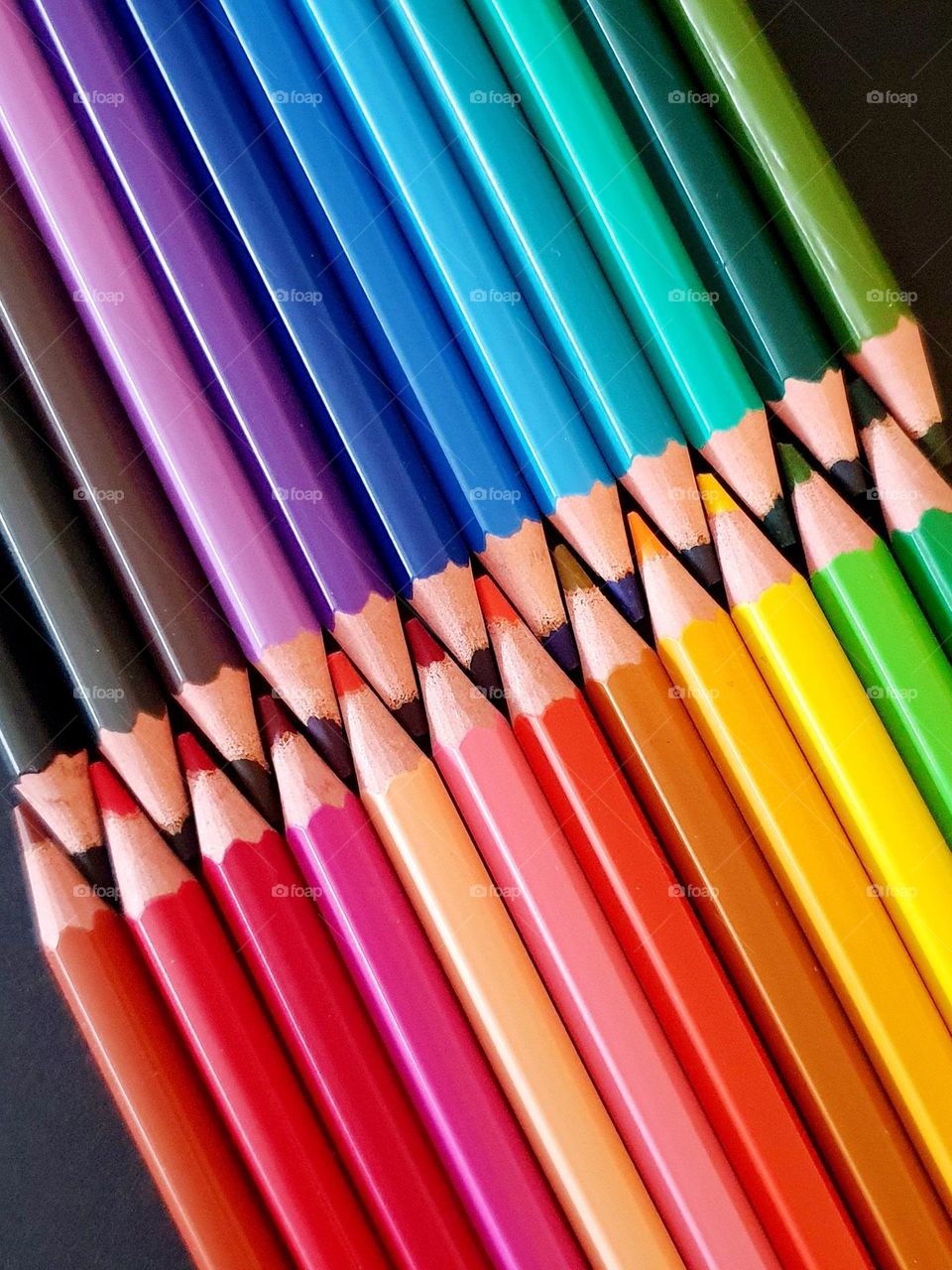 Primary colours flatlay composed of colour pencils placed on black paper and showing two rows of pencil leads interlocked