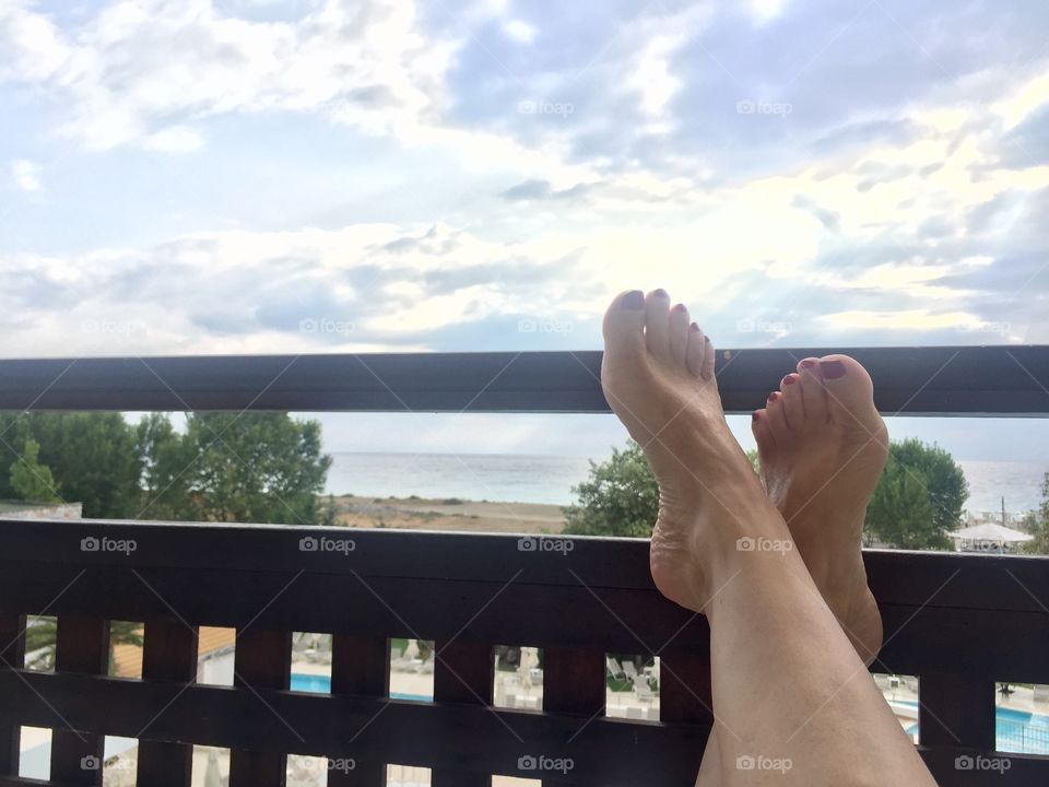 Woman resting with her feet on the balcony railing in resort in Greece