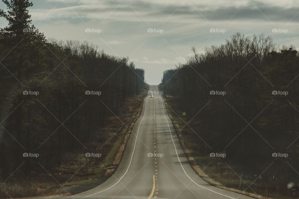 A long road going into the distance, a single car driving, large forest on both sides of the road