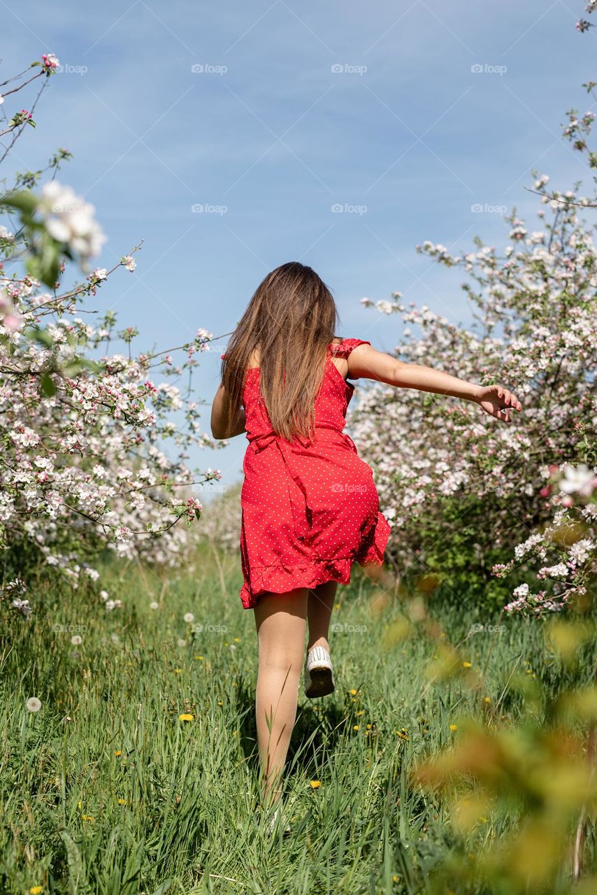 back view woman in red dress dancing in blossom trees