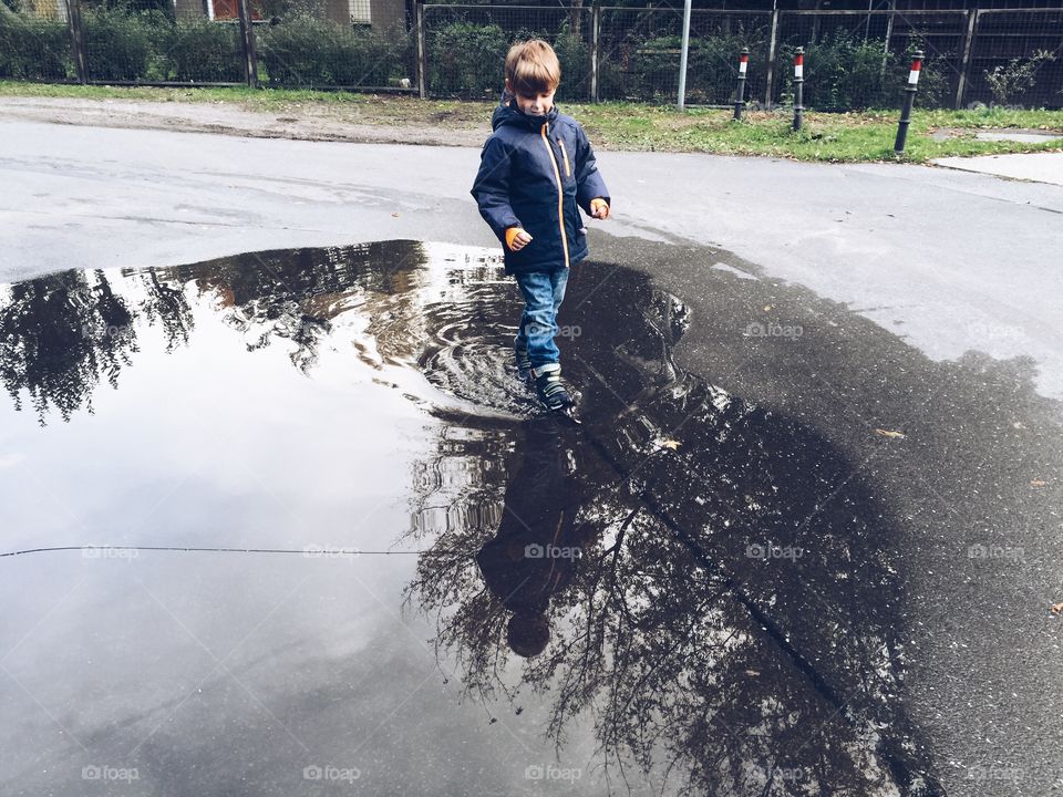 Boy walking through puddle. Boy walking through a huge puddle with sky reflections
