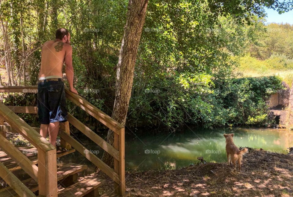 A man and his dog relax and prepare for a dip at a shady waterhole during a heatwave in Portugal - July 2022