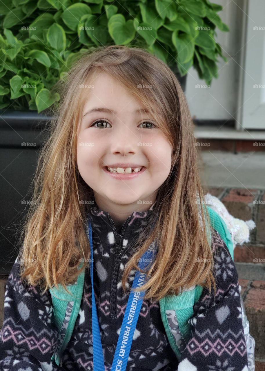 Patiently waiting for the bus with an oversized bookbag and a big smile.