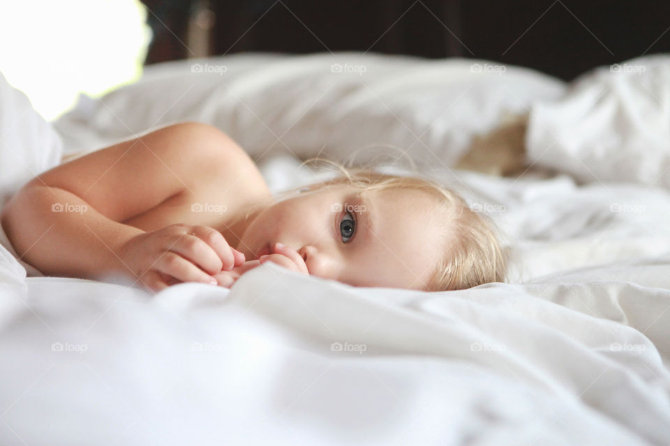 Sweet and adorable little blonde baby sucking her thumb and laying on her side with the most peaceful expression. 