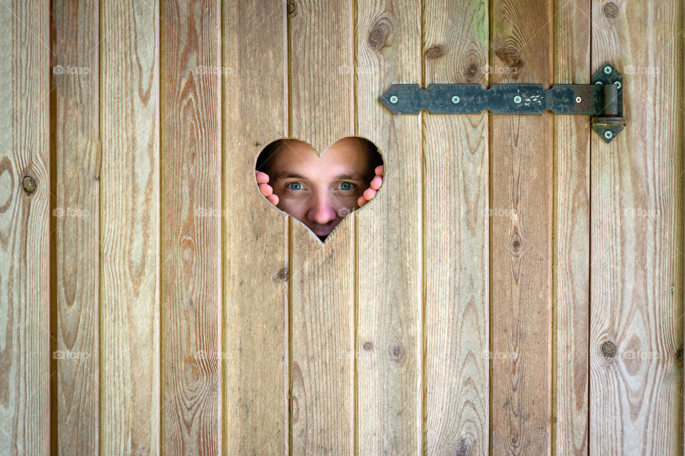 Wooden outdoor toilet with heart shape on the door. A man looking through a heart-shaped window.