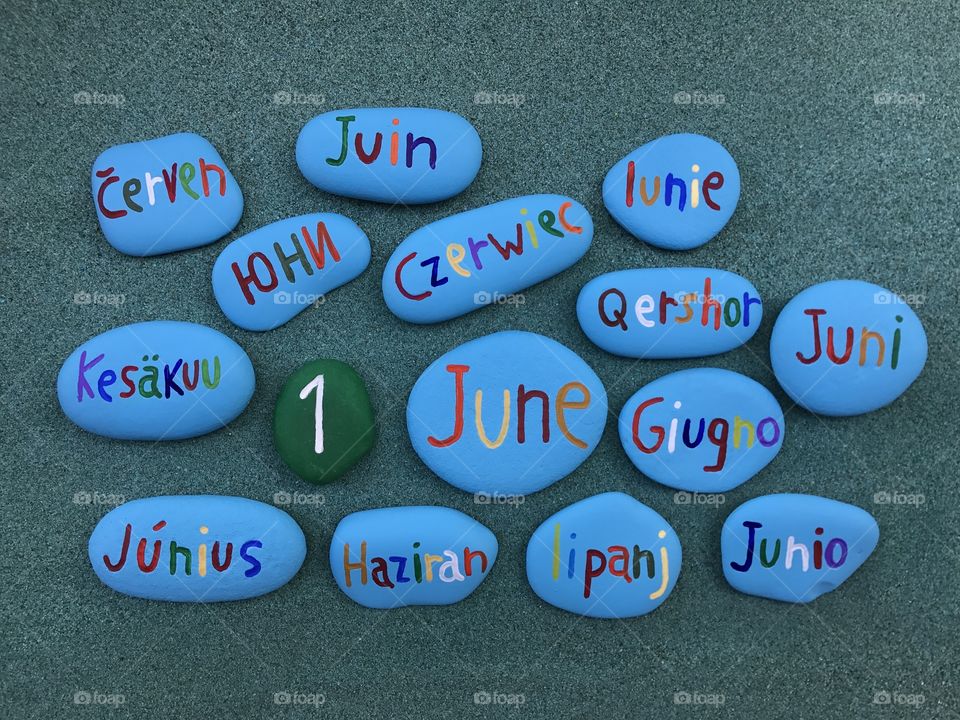 1 June in many languages with painted stones over green sand 