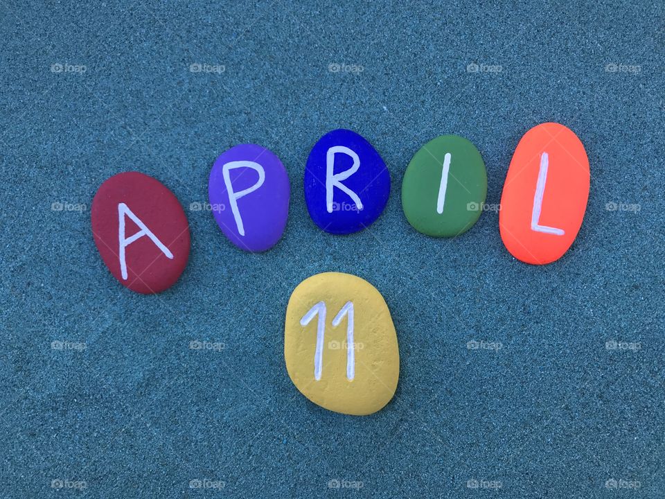 11 April, calendar date with colored stones over green sand 