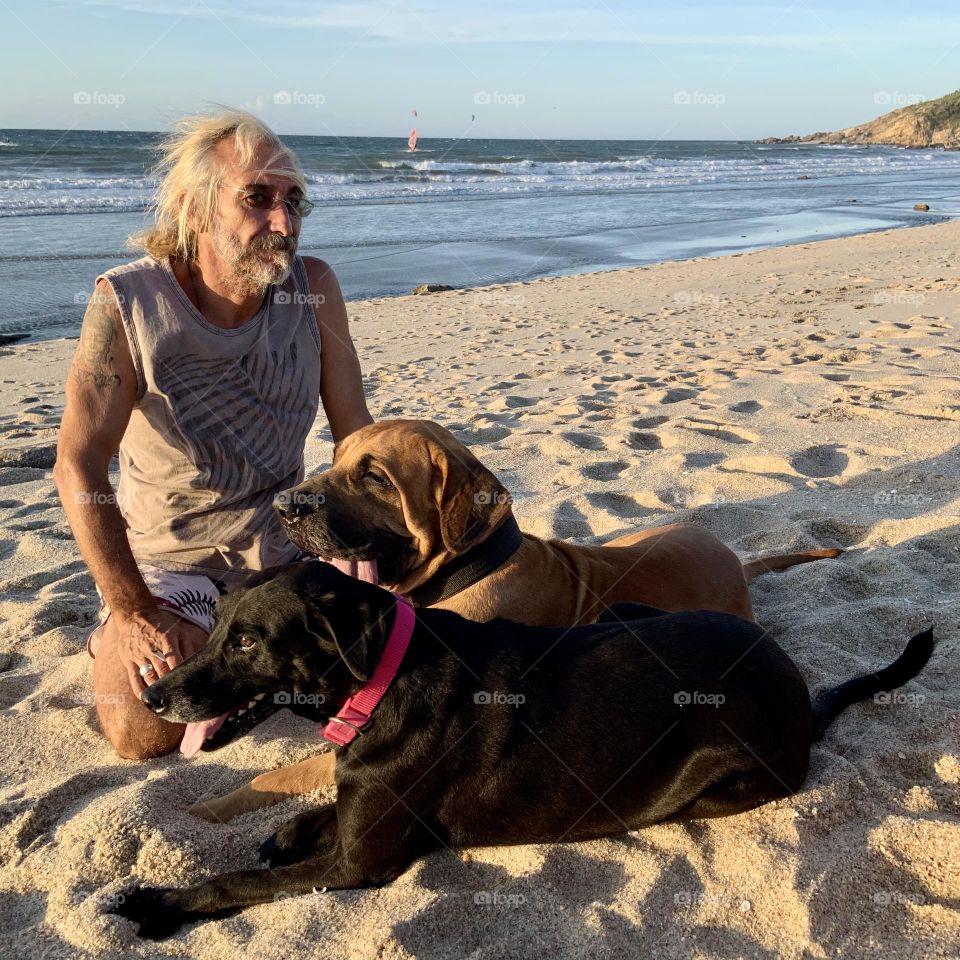 Mature man with beard sitting in the beach with dog 