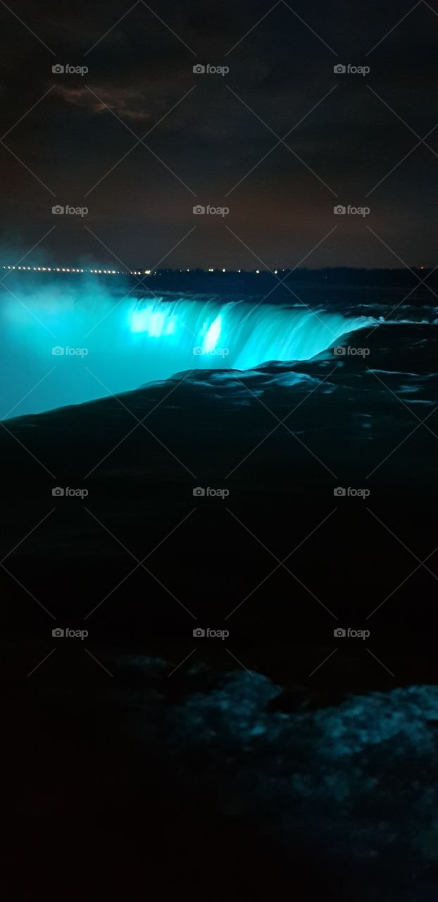water rushing off the edge of Niagara Falls at night lit up by blue light