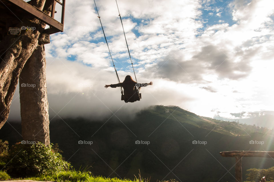 Woman swinging on a tree swing at the edge of a cliff at sunset 