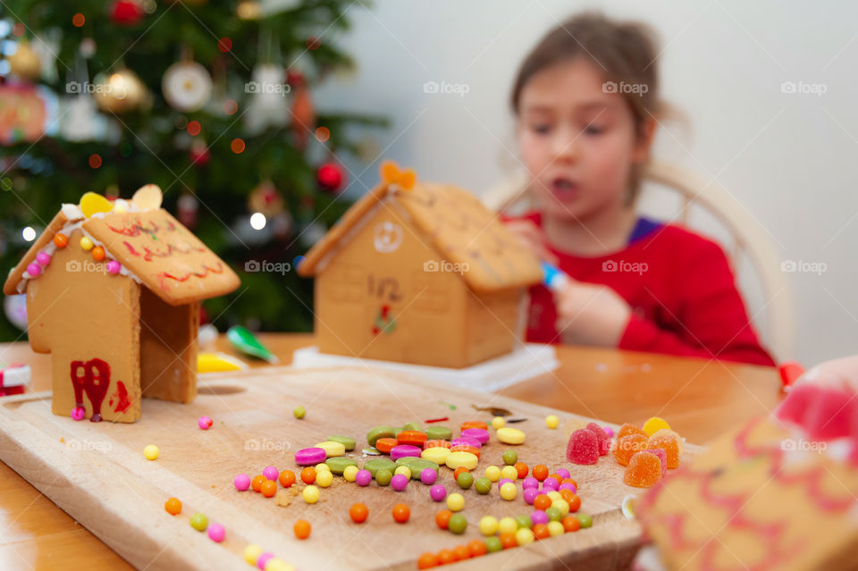 Girl decorating her gingerbread house with colorful sweet pastilles and sparkling glitter.