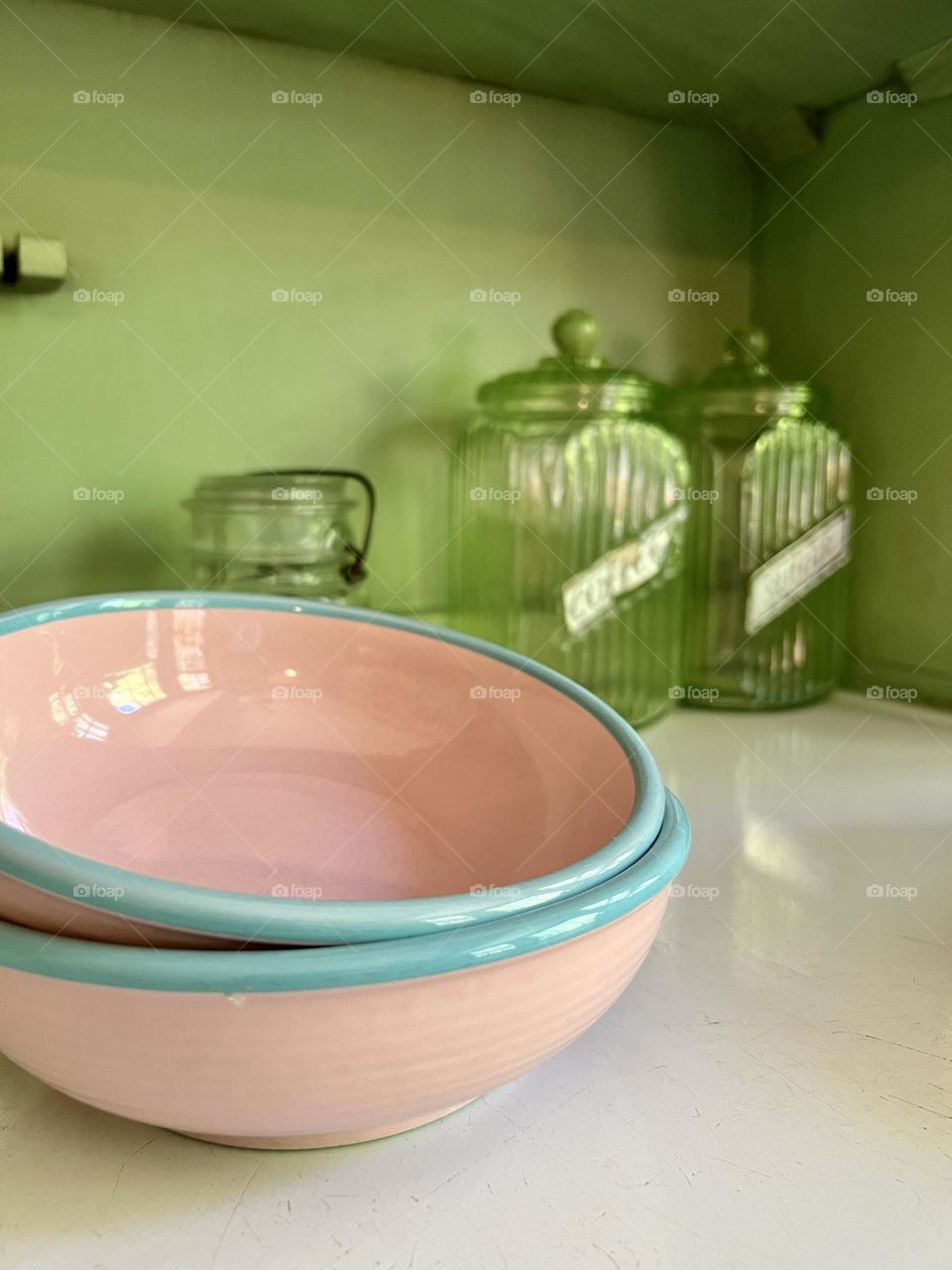 Antique ceramic pink bowls with baby blue rims on an antique green cupboard with glass containers in the background 