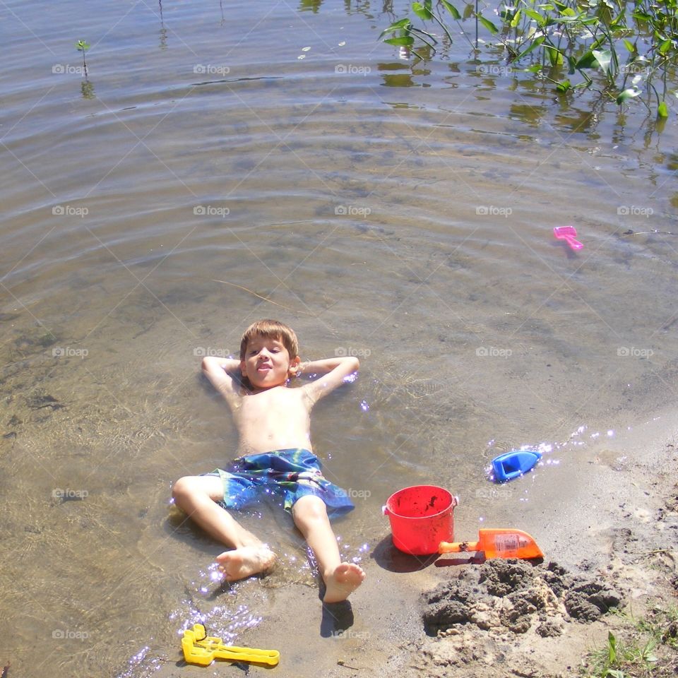 Young boy laying on his back on the lakeshore.