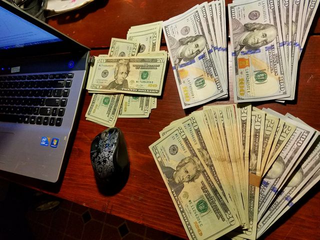 U.S. Paper currency spread out near laptop, adding up paper money on desk. $20s & $100s.