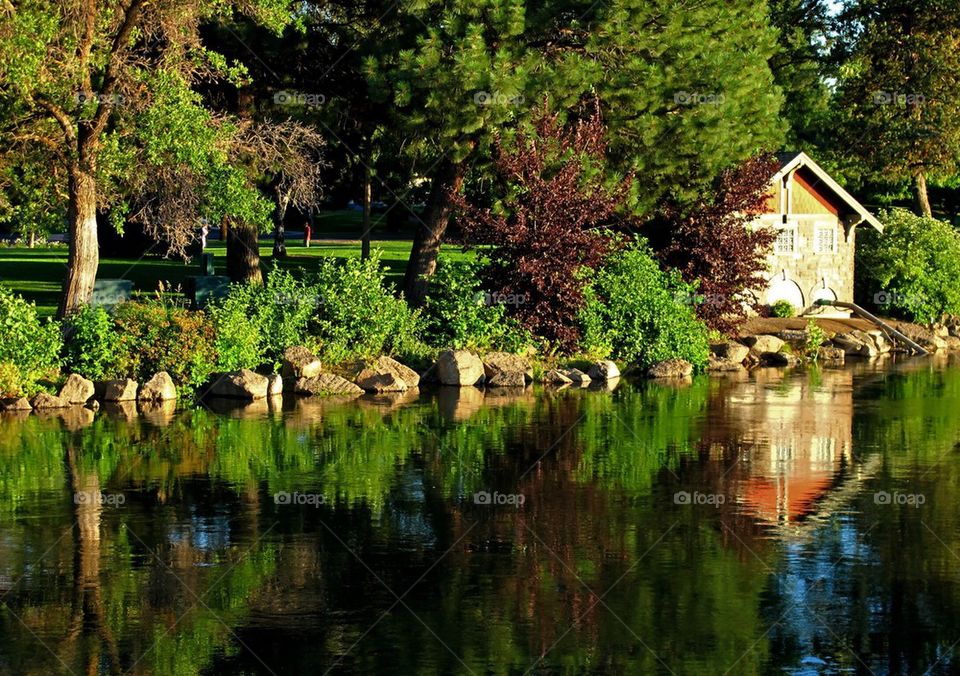 Trees, bushes, the sky, and a pump house produce beautiful reflections in the Deschutes River at Drake Park in Bend in Central Oregon on a sunny summer day. 