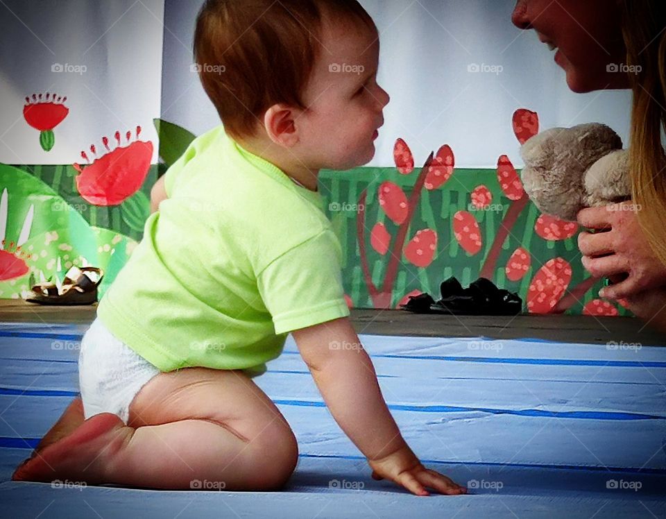 Small children.  A boy in a diaper sits on the stage and smiles at his mother.  The first love